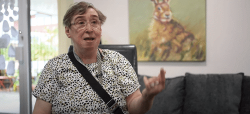 A woman wearing glasses and a white and black spotted top sitting in a chair.