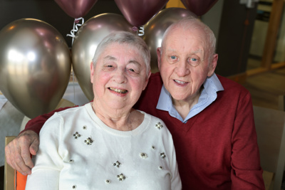 A woman and man hugging each other with some balloons behind them