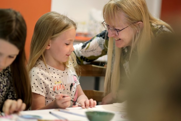 A woman smiling at a young girl as they do craft activities.