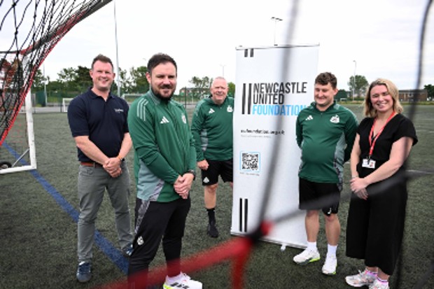 Four men and one woman standing behind a football net next to a Newcastle United Foundation sign