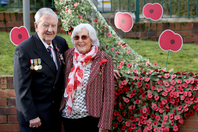 A man and woman standing next two each other with a collection of poppies behind them