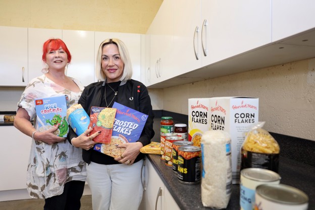 Two women standing in a kitchen holding various food items.